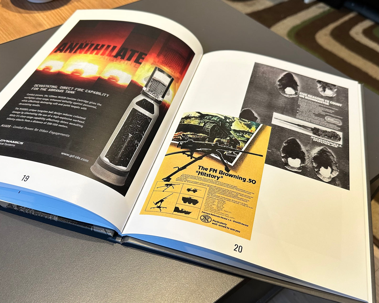 A photo from The Warfare Media Collection - Photo Book by Warfare Media shows an open book resting on a table, with pages 19 and 20 clearly visible. Page 19 displays an advertisement for a grenade-like device, reminiscent of Cold War propaganda, while page 20 features a yellow and black recruitment poster with aviation-related content and a grayscale image of two faces.