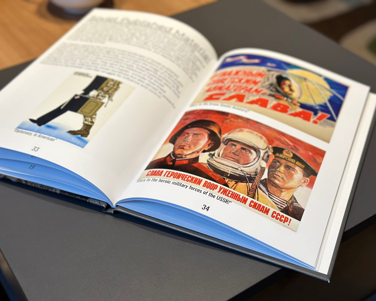 A volume from The Warfare Media Collection - Photo Book by Warfare Media lies open on a dark table. One page showcases text alongside an image of a gun, while the opposite page features a vibrant illustration of three individuals in space suits adorned with Russian text above and below, evoking the style of Cold War propaganda. The pages are numbered 33 and 34.