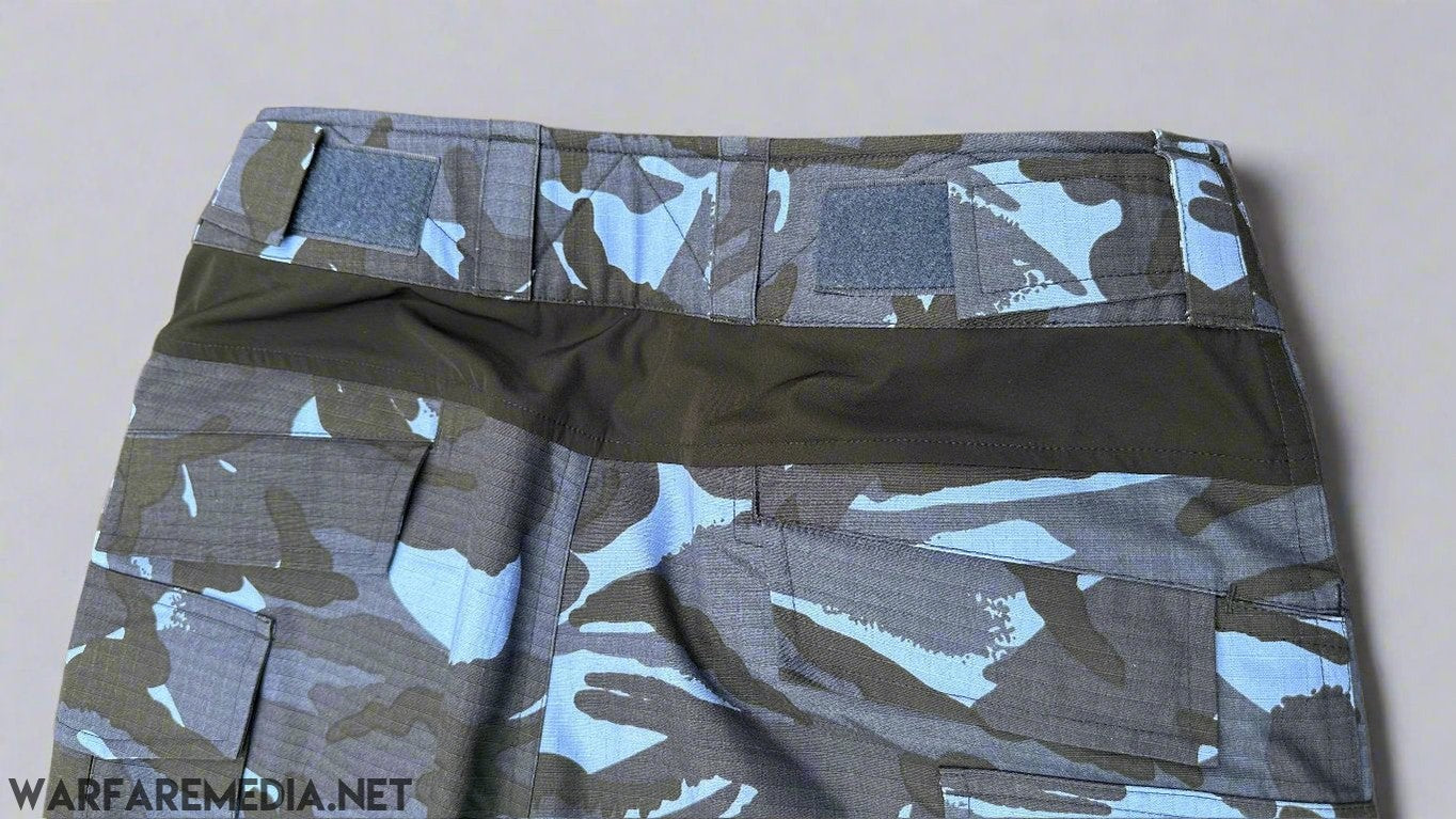 A close-up image of the waist and upper part of Warfare Media's OPFOR DPM Trousers (G3 Cut) in a blue and black camouflage pattern, showcasing Velcro patches and multiple pockets. These trousers are perfect for tactical training or OPFOR DPM scenarios and are laid flat on a brick surface.