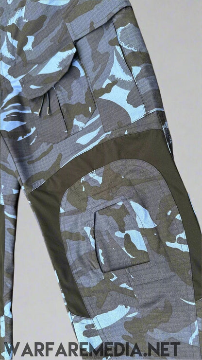 A close-up image of Warfare Media's OPFOR DPM TROUSERS (G3 Cut) with a blue, grey, and black camouflage pattern. The pants are laid out on a brick surface, showcasing design elements like multiple pockets and reinforced knee sections, perfect for tactical training or OPFOR DPM scenarios.