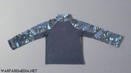 The Warfare Media OPFOR DPM UBACS (G3 Cut) with a dark blue body and OPFOR DPM patterned sleeves is laid flat on a brick pavement. The shirt features a quarter-zip neckline. The bricks underneath vary in reddish and brownish hues, accented with patches of green moss between them.