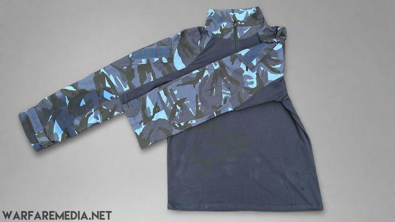 A long-sleeve OPFOR DPM UBACS (G3 Cut) shirt from Warfare Media lies spread out on a brick pavement. The shirt features a dark gray lower section and sleeves with a blue and black camouflage pattern reminiscent of OPFOR DPM. The high collar also displays the same camouflage design, offering tactical flair for body armor integration.