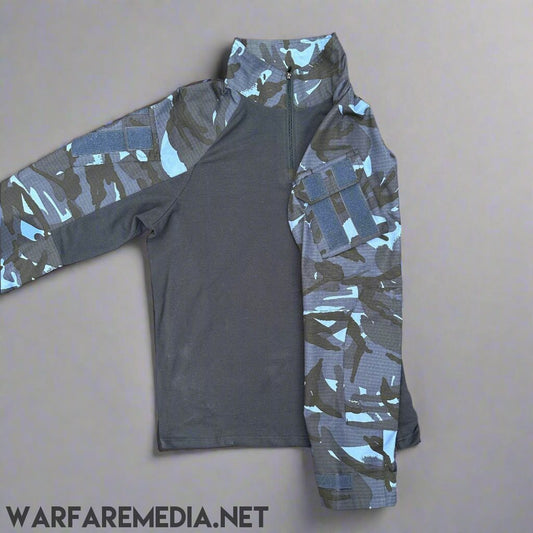 The Warfare Media OPFOR DPM UBACS (G3 Cut) shirt is displayed on a brick pavement. It features a solid dark gray torso with blue and gray OPFOR DPM pattern sleeves and shoulders, a high collar with a partial front zipper, and a pocket on the left sleeve. The shirt also has long sleeves.